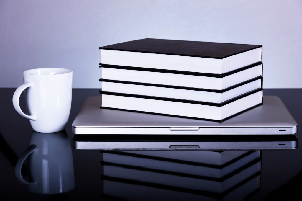 Laptop books, coffee mug on a reflective surface