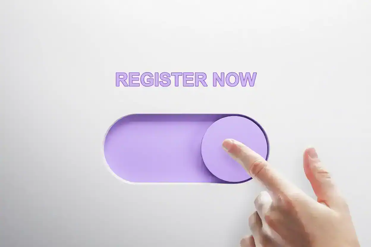 Hand pressing a large purple “Register now” button on a light gray background.