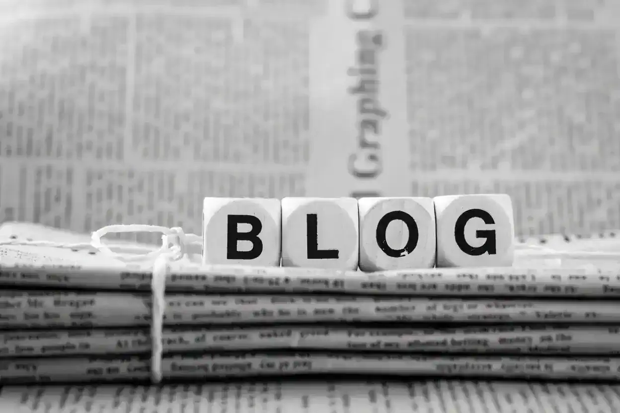 Wooden letter blocks spelling “BLOG” on top of a stack of newspapers.