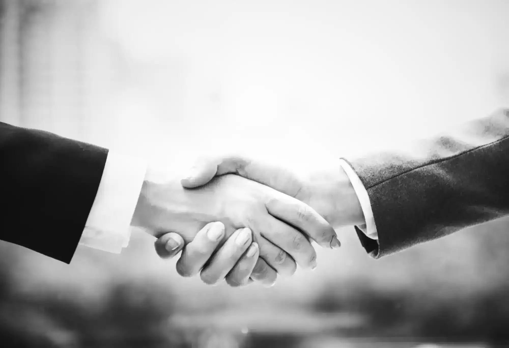Two people in business attire shaking hands in a black-and-white photo.