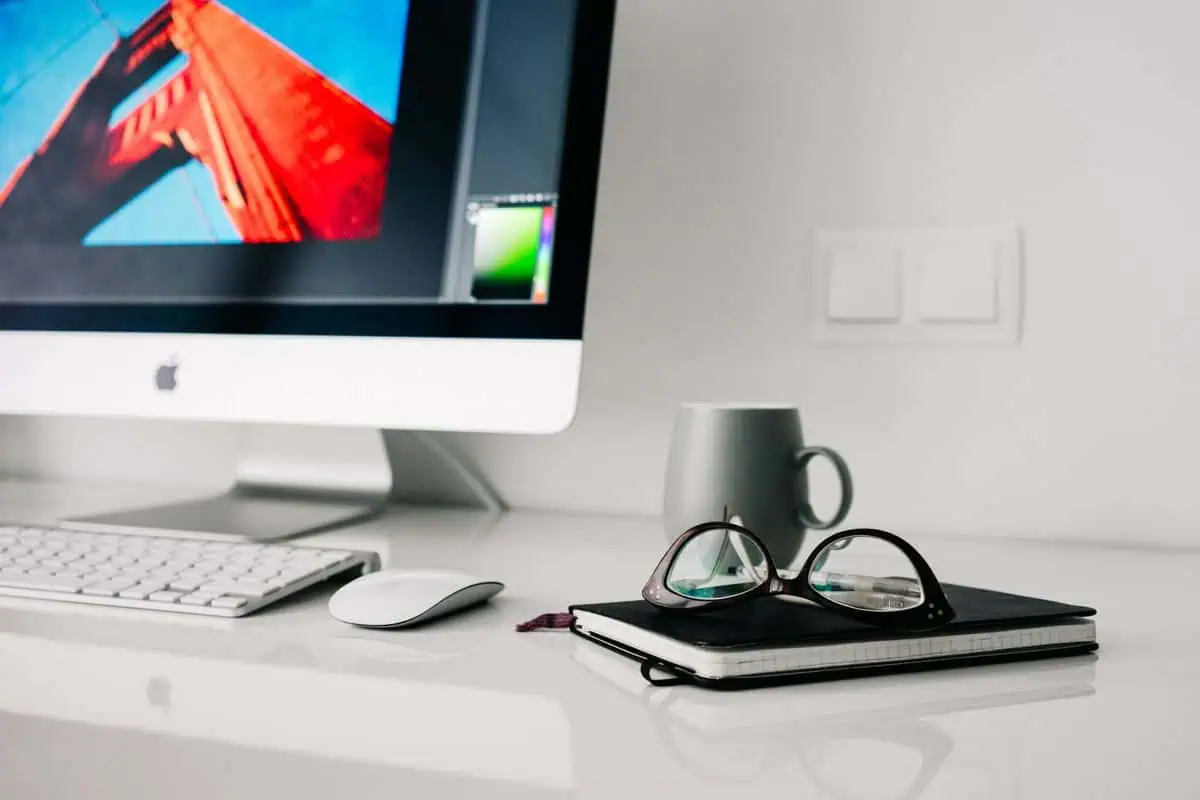 Stylish office workspace featuring a desktop computer, glasses, and notebook.